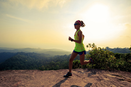 Young woman running on mountain top rockの写真素材