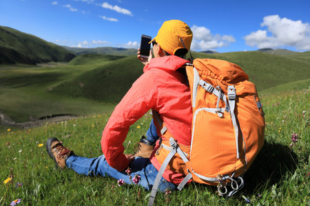 young woman taking photo with smartphone hiking in prairie mountains