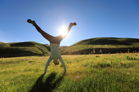 woman doing a handstand in a sunrise meadowの写真素材