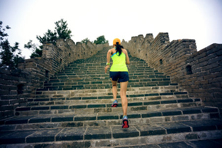 young woman trail runner running at great wall on the top of mountain