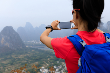 successful backpacker taking photo with smartphone on the top of  mountainの写真素材