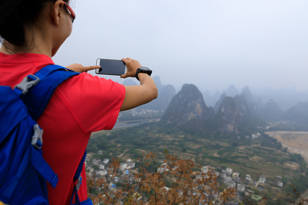 successful backpacker taking photo with smartphone on the top of  mountainの写真素材