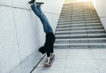 female skateboarder doing a handstand on skateboard against wall