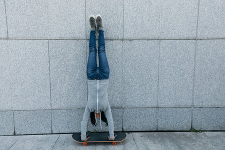 female skateboarder doing a handstand on skateboard against wall