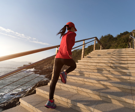 sporty fitness female runner running upstairs on coast trailの写真素材