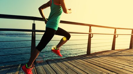 sporty fitness female runner running on seaside boardwalk during sunriseの写真素材