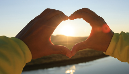 Human hands making Heart shaped sign over sunset skyの写真素材