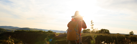young woman photographer taking photo on sunset mountain topの写真素材