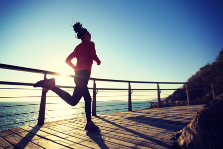 sporty female jogger morning exercise on seaside boardwalk during sunriseの写真素材
