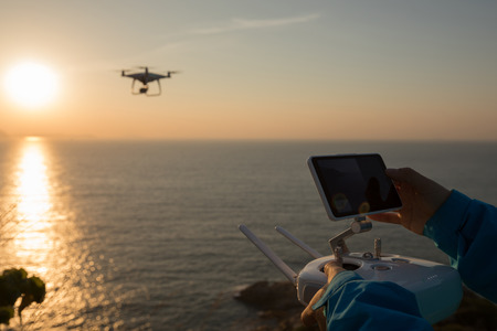 Silhouette of remote controlling a flying drone which taking photo over sunrise seaの写真素材