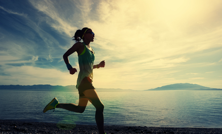 Young fitness sporty woman running on rocky seasideの写真素材
