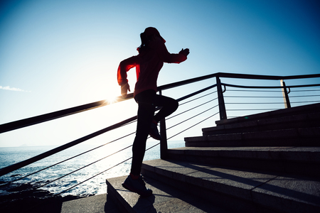 sporty fitness female runner running upstairs on coast trailの写真素材