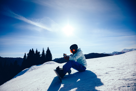 one snowboarder use smatphone on winter mountain topの写真素材