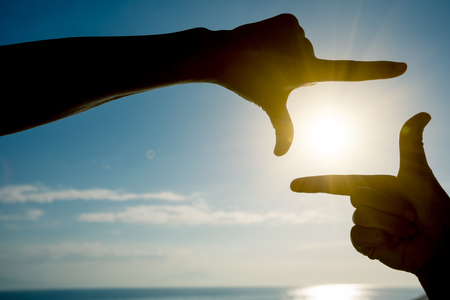 Fingers gesturing picture frame on sunrise seasideの写真素材
