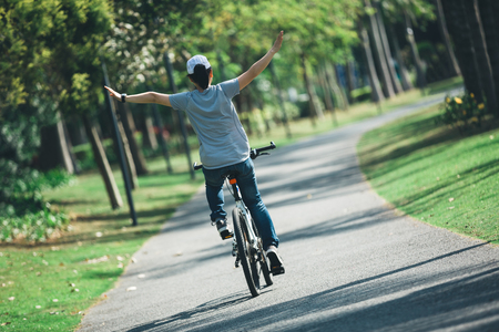 happy woman cyclist riding bike on tropical parkの写真素材