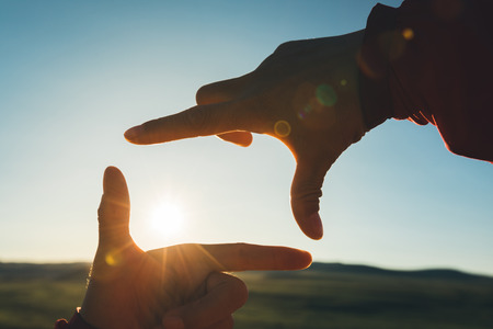 Human hands making a frame sign over sunset sky の写真素材