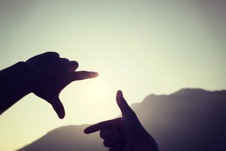 Hands making a  picture frame on  mountain top with sunlights behind