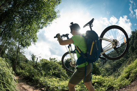 Female Cyclist carrying mountain bike on mountain trailの写真素材