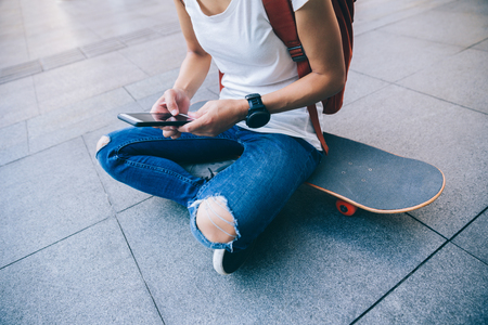 Skateboarder use smartphone sit on skateboard on city streetの写真素材