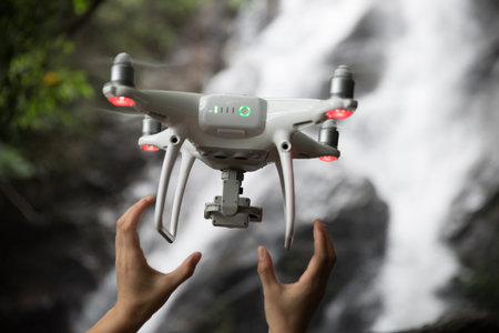 The UAV drone and photographer hands near waterfall