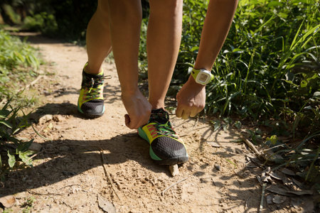 Young fitness woman runner tying shoelace on forest trail