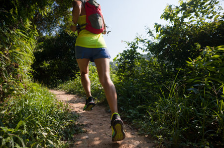 Young woman trail runner running on tropical forest trail