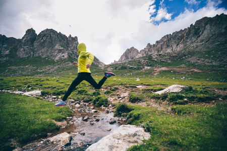 Woman trail runner jumping over small river on mountainsの写真素材