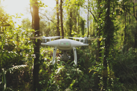 White drone with camera flying in tropical forest