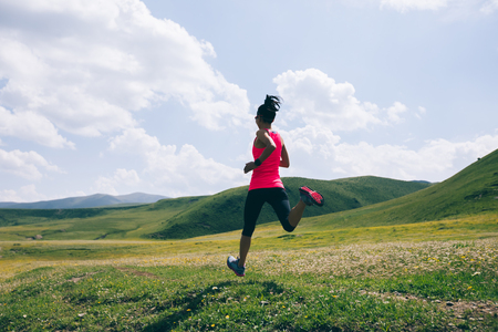 Young fitness woman trail runner running grasslandの写真素材