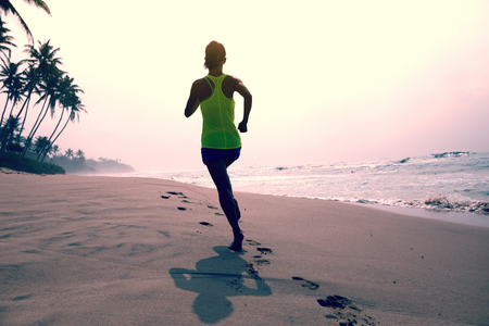 Fitness healthy lifestyle young woman running on tropical beach during sunrise in the morningの写真素材