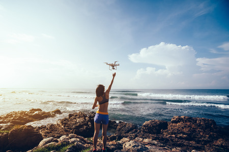 Woman photographer landing or taking off a drone on seasideの写真素材