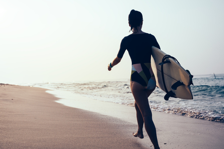 Surfer woman with surfboard walking on tropical beachの写真素材