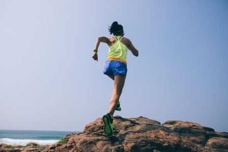 Young fitness woman trail runner running to rocky mountain top on seasideの写真素材