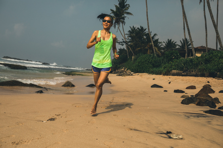 Fitness healthy lifestyle young woman running on tropical beach during sunrise in the morningの写真素材