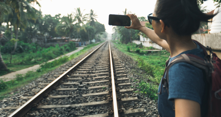 Woman tourist using mobile phone taking photo of rail wayの写真素材