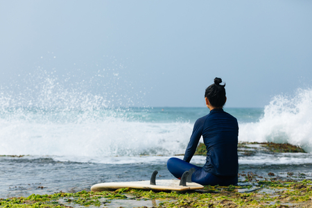 woman surfer sit on reef looking at the wavesの写真素材