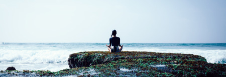 Woman meditation at the seaside croal cliff edge facing the coming strong sea wavesの写真素材