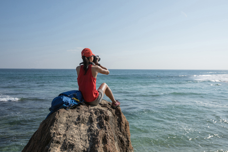 woman photographer taking photo sit on seaside rock cliff edgeの写真素材