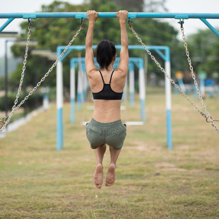 Fitness asian woman doing pullups at outdoor fitness park, healthy lifestyle concept.