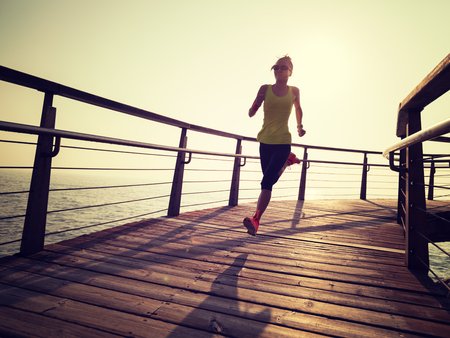 sporty fitness female runner running on seaside boardwalk during sunriseの写真素材