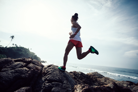 Woman trail runner running at rocky mountain top on seasideの写真素材