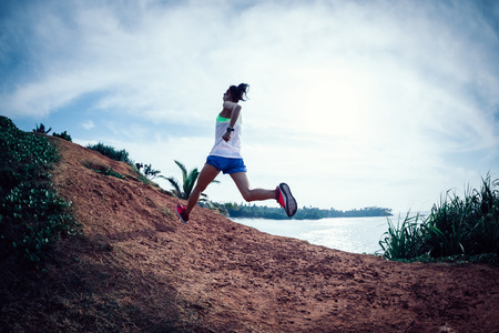 Woman trail runner running on seaside hillsの写真素材
