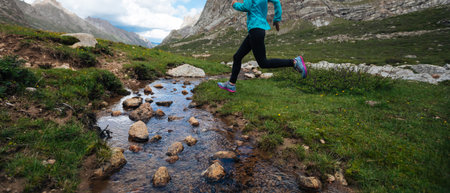 Woman trail runner jumping over small river on beautiful mountains