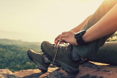 Successful hiker sit and tying shoelace on mountain peak cliff edgeの写真素材