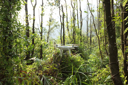 White drone with camera flying in tropical forest
