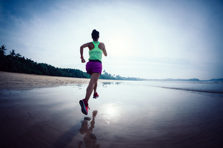 Fitness woman runner running on sunrise beachの写真素材