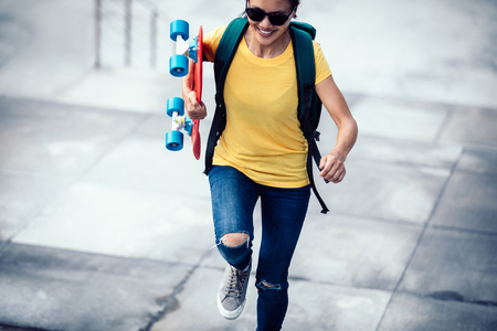 Woman skateboarder walking with skateboard in hand at city stairsの写真素材