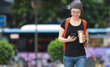 Woman looking at mobile phone while walking with bottle in handの写真素材