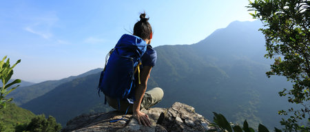 Successful woman backpacker sit on cliff edge at mountain top