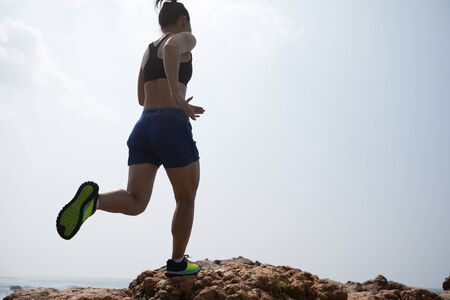 Woman ultramarathon trail runner running to rocky mountain top on seasideの写真素材